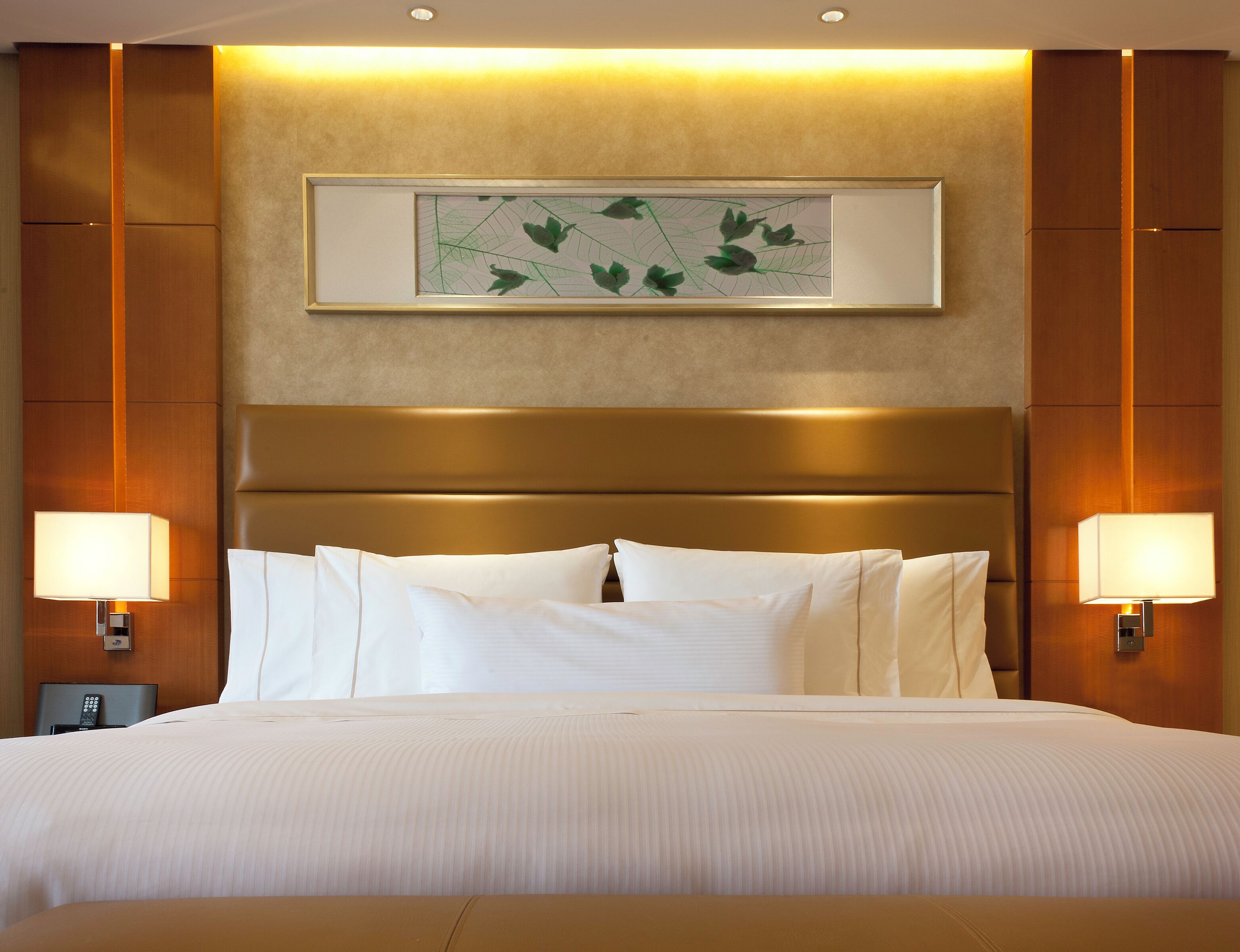 Une chambre d’hôtel avec un grand lit, deux lampes de chevet, une œuvre d’art encadrée au mur et une tête de lit en bois.
