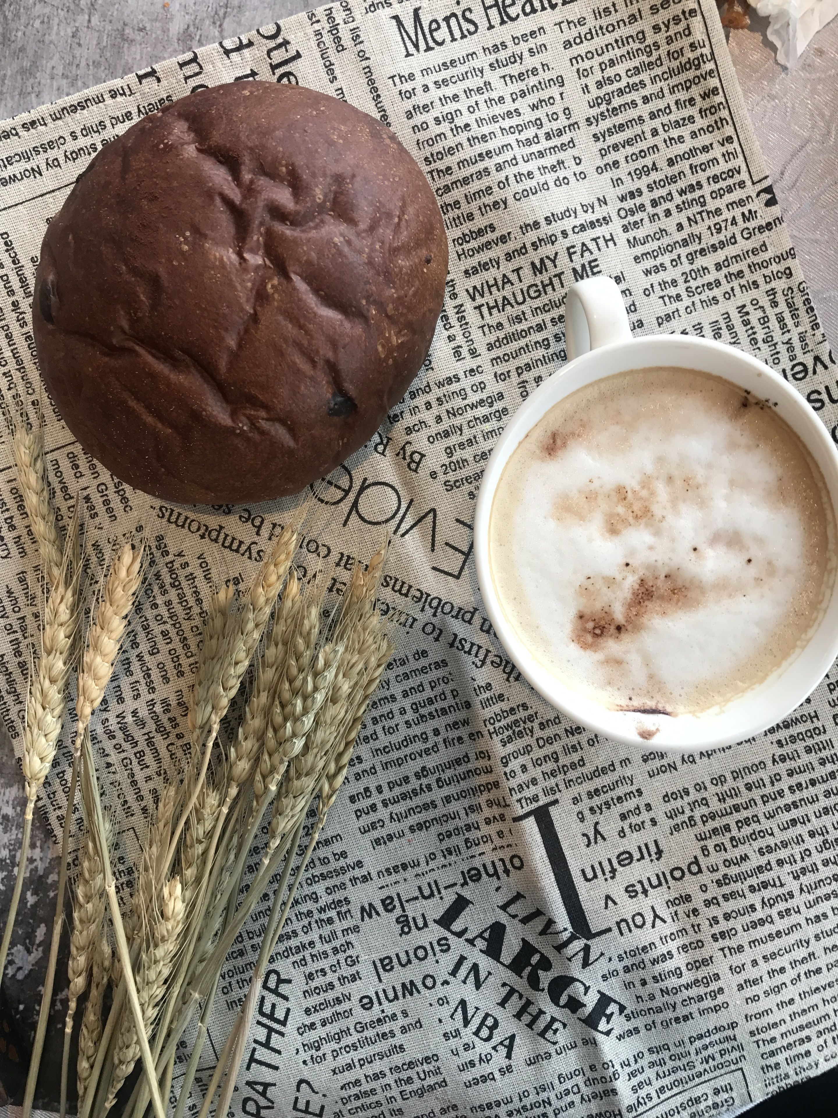 A muffin, a cup of coffee, and wheat stalks on a newspaper.