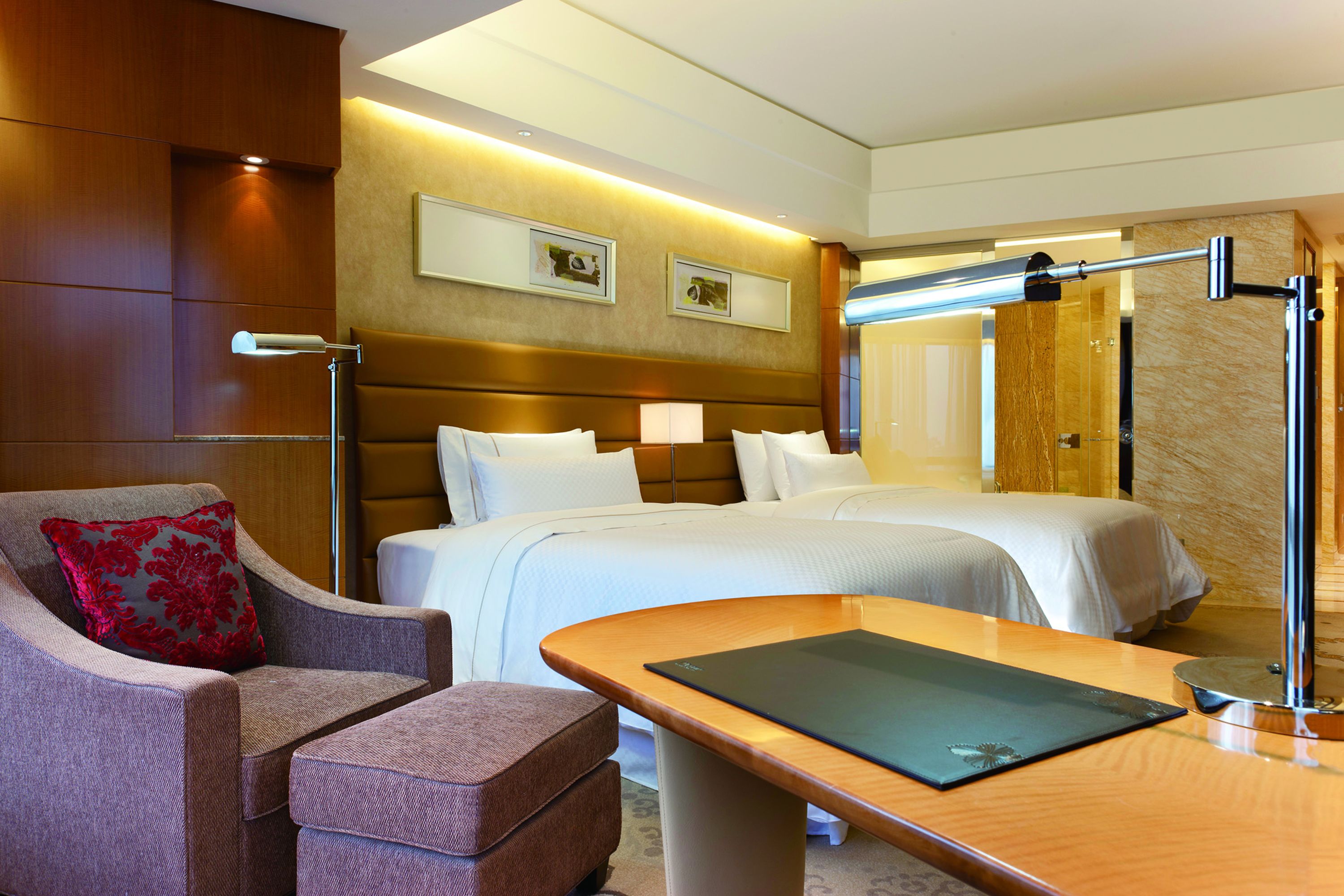 A hotel room with a bed, a desk, a chair, and a lamp.