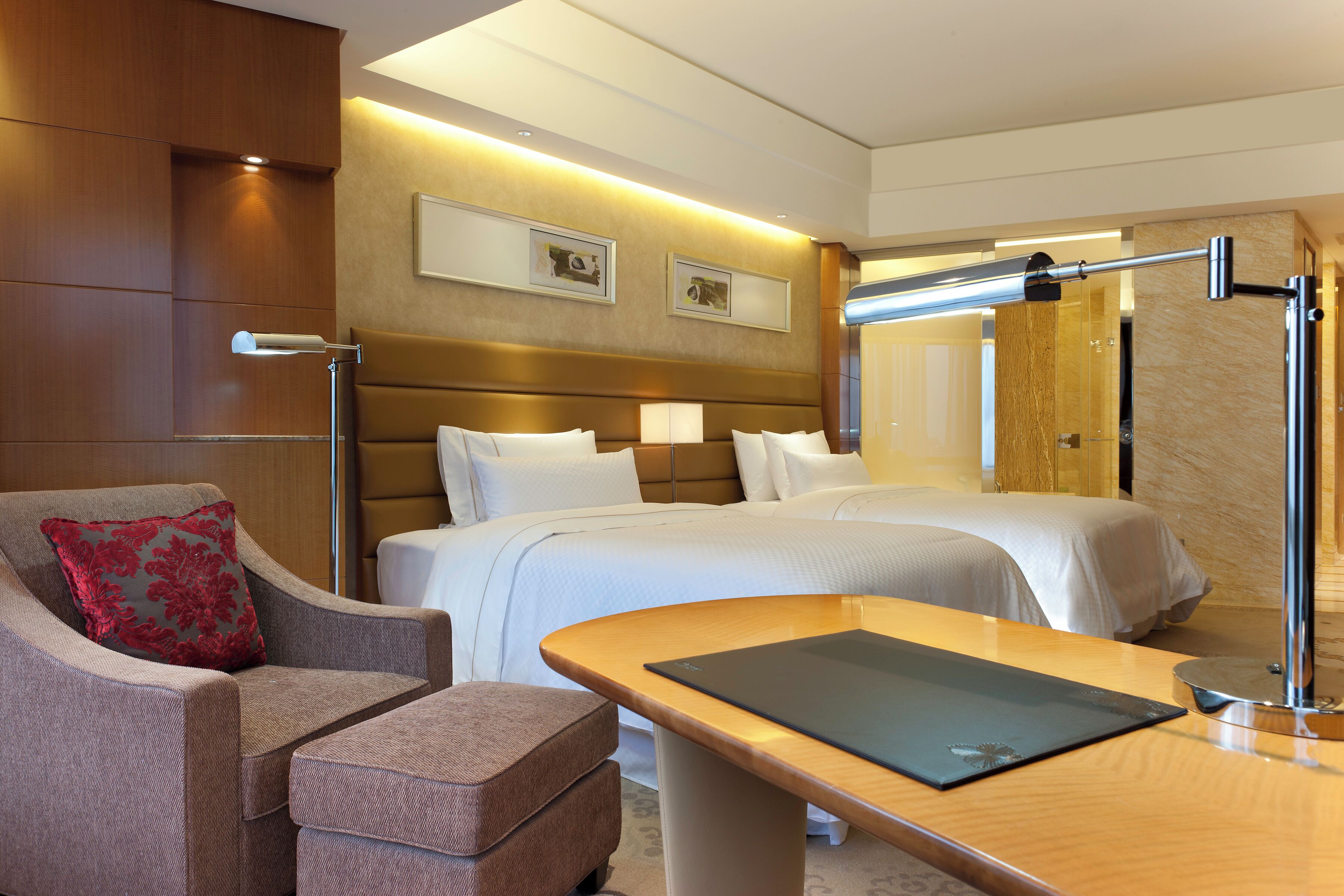 A hotel room with a bed, a desk, a chair, and a lamp.