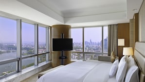 A hotel room with a large bed, a flat-screen TV, a city view, and a large window.
