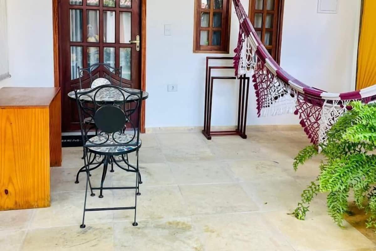 Un patio couvert avec une table et des chaises en bois, un hamac et une petite table avec une lampe.