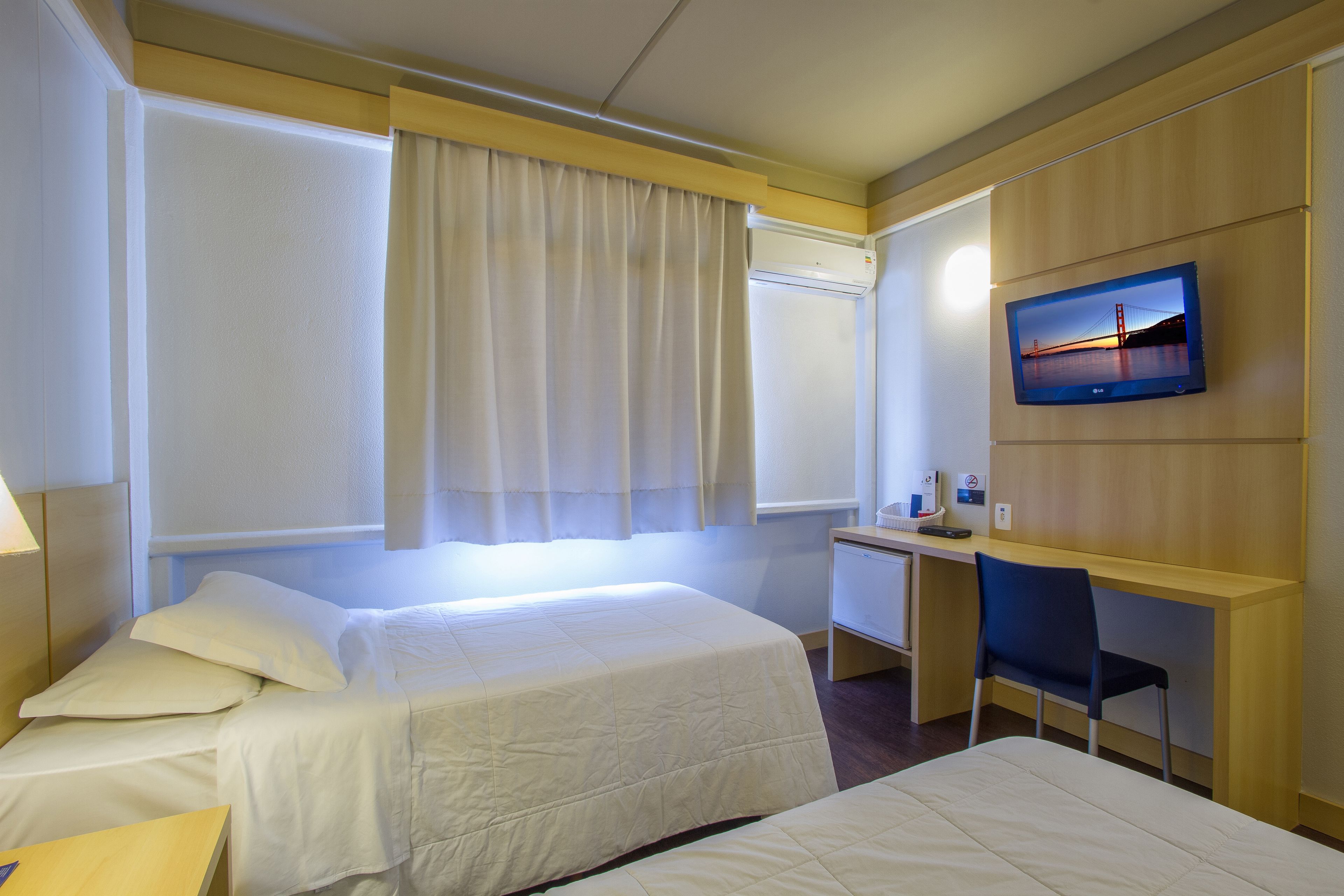 Habitación de hotel con dos camas, un escritorio, una silla, un televisor y una ventana con cortinas.