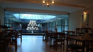 A spacious dining area with wooden tables and chairs, a chandelier, and a large glass window offering a view of the interior. - Hotel Águas Virtuosas (Lambari)