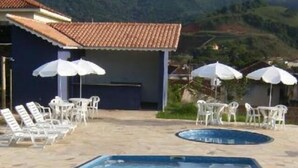 A swimming pool with lounge chairs and umbrellas, surrounded by a mountainous landscape. - Hotel Águas Virtuosas (Lambari)