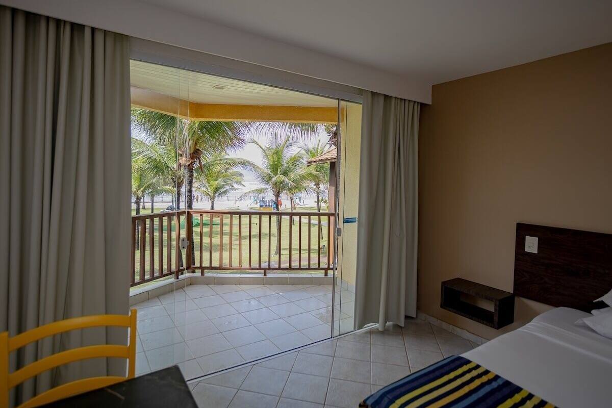 A hotel room with a balcony, a bed, a chair, and a small table.