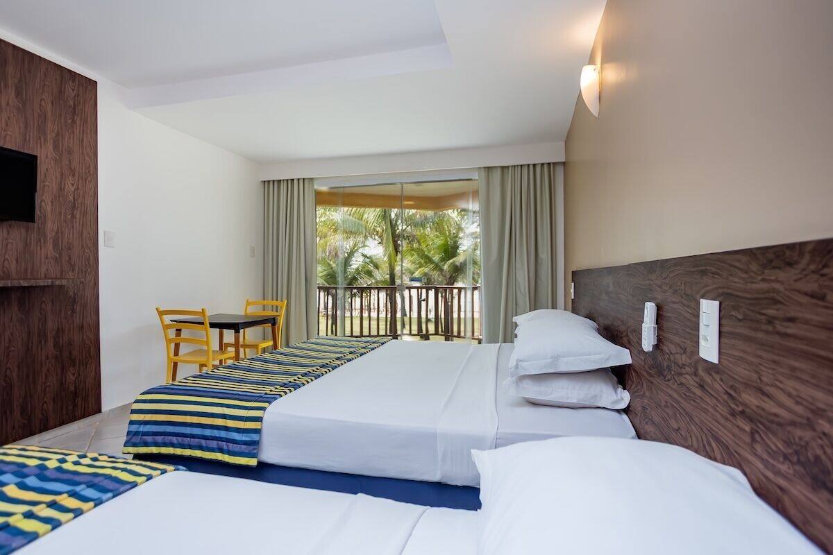 A hotel room with two beds, a TV, a balcony with curtains, and a table with chairs.