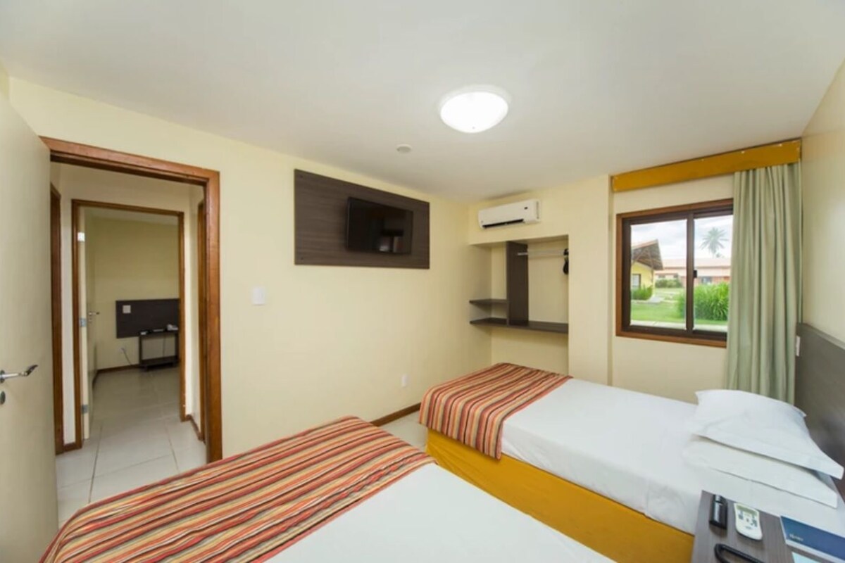 A hotel room with two beds, a desk, a TV, and a window with curtains.