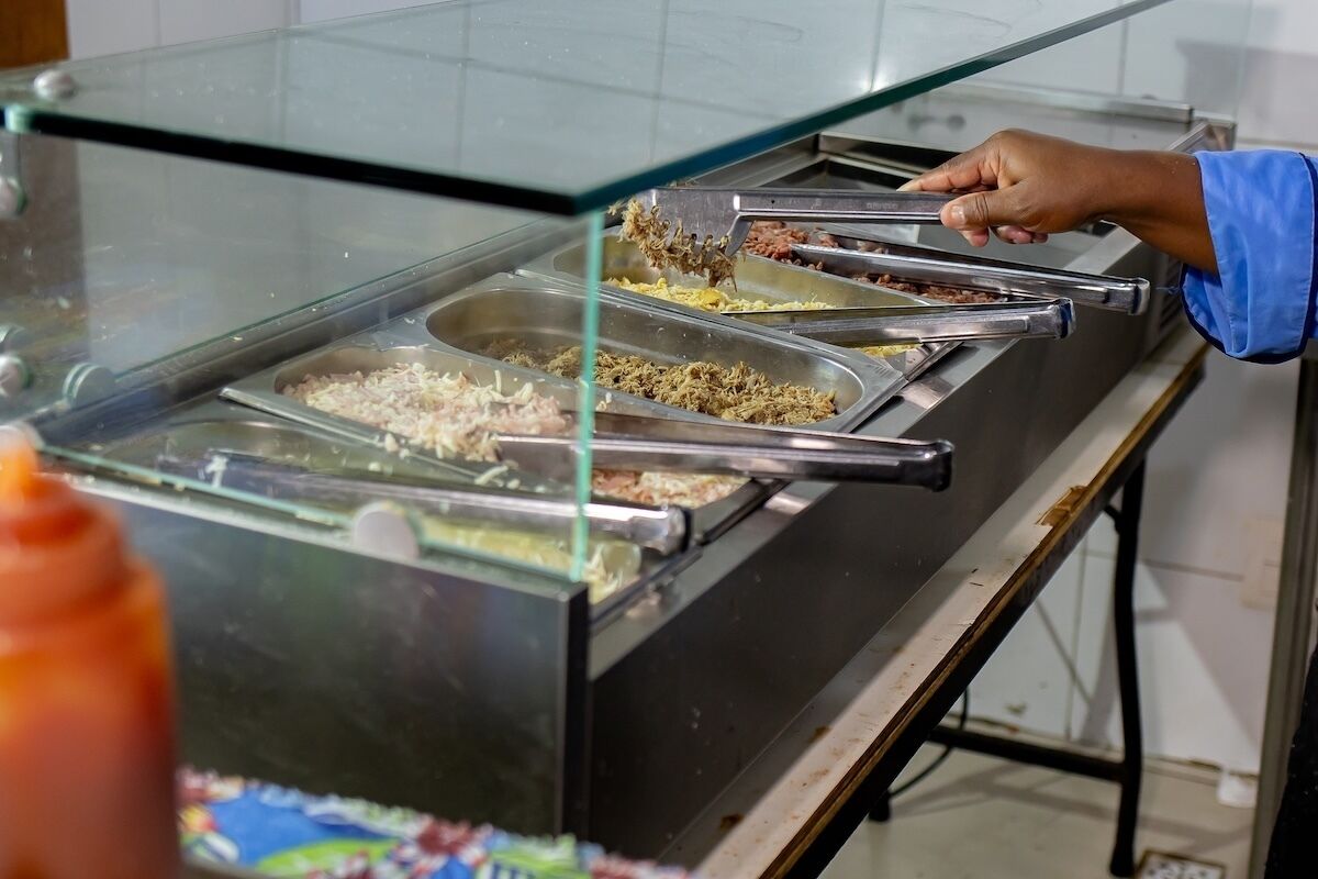 Buffet com várias bandejas de comida e uma pessoa servindo.