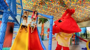 Ein Spielbereich mit Rutsche, Spielgeräten aus Netz und einer großen Maskottchenfigur.