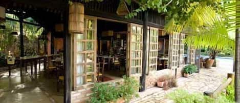 A cozy, rustic-style building with a stone-paved entrance, wooden furniture, and lush greenery.