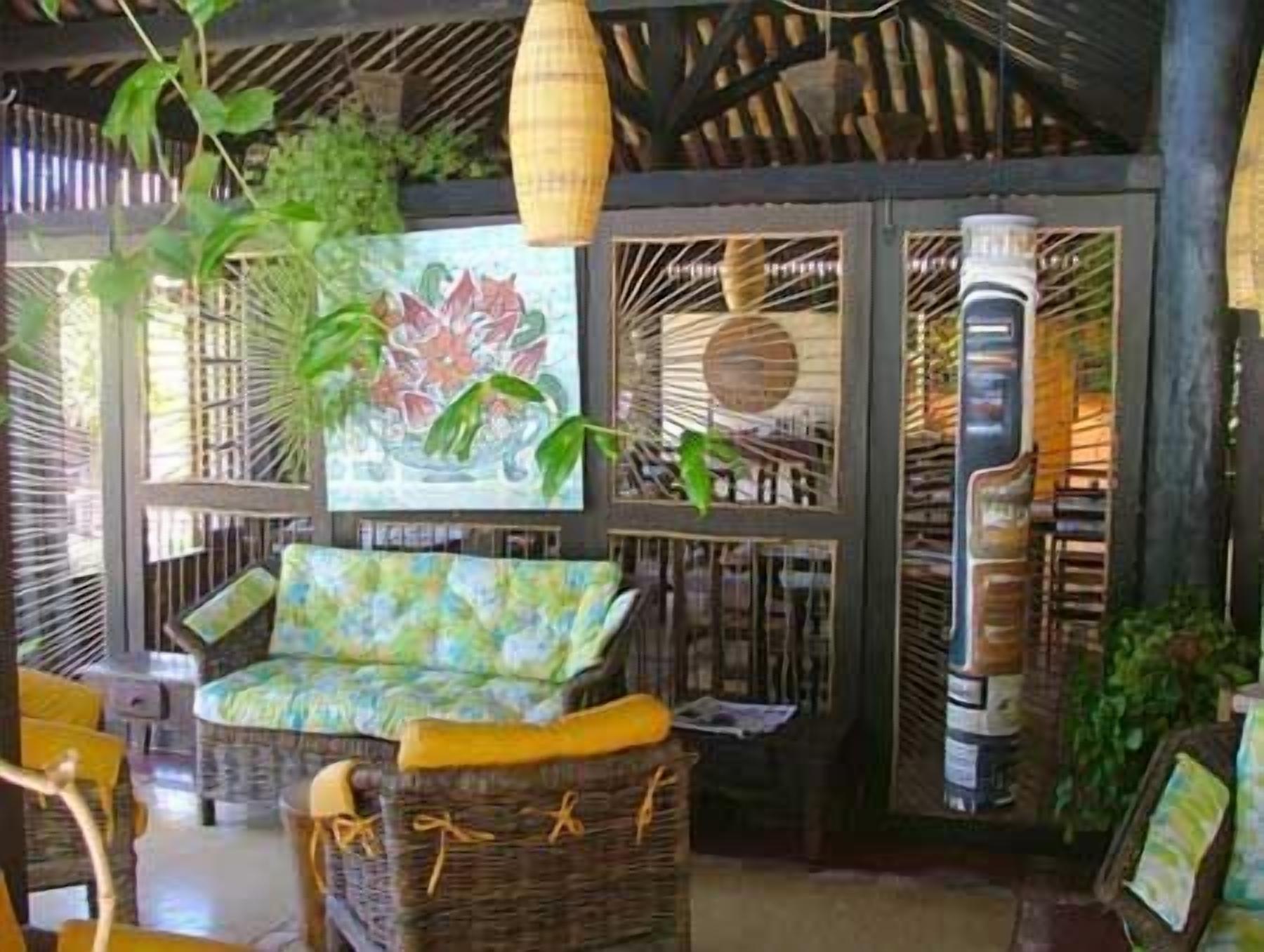 A room with a wicker sofa, a chair, and a table. There are plants and a painting on the wall.