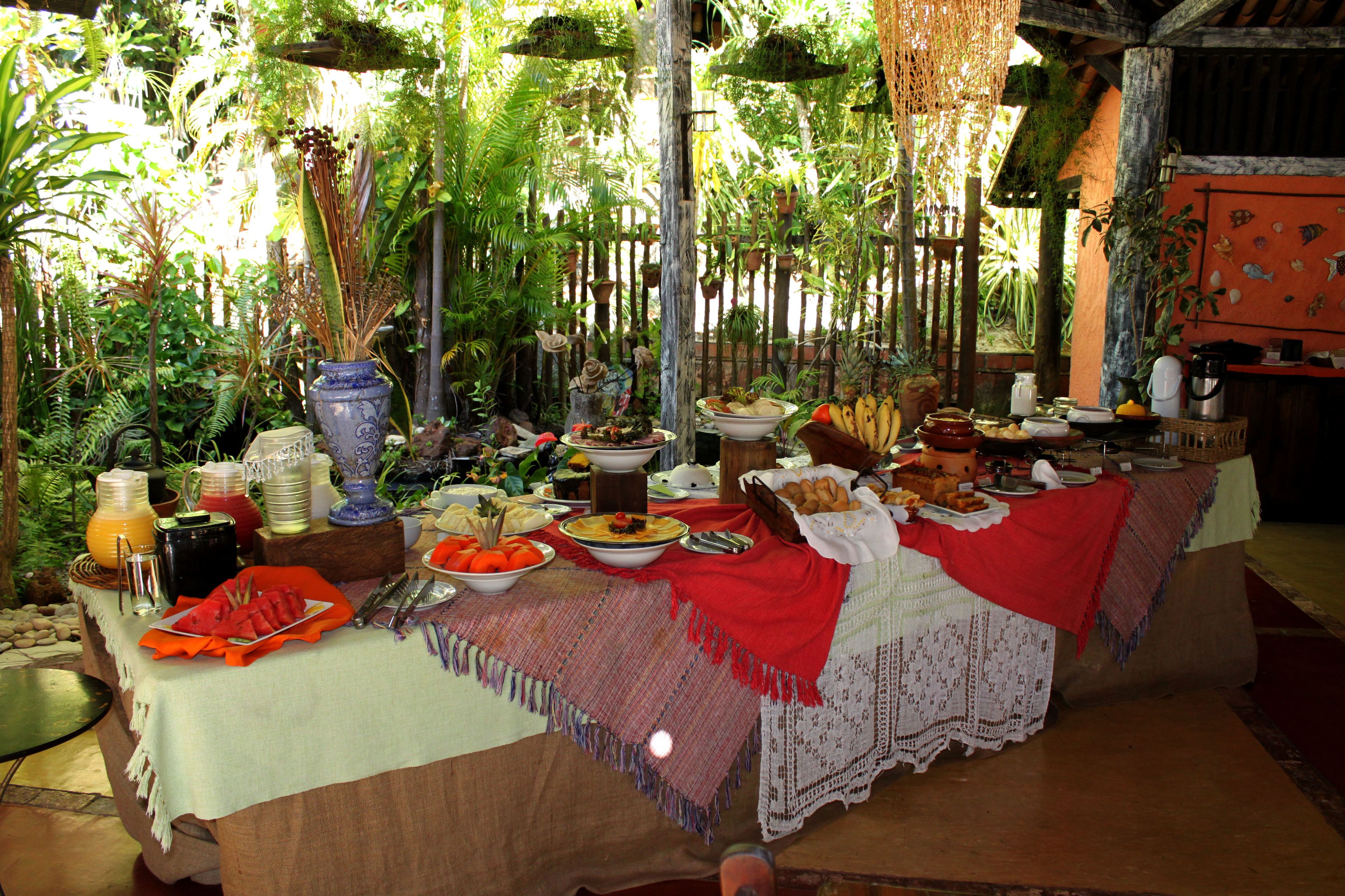 Una larga mesa de comedor dispuesta con diversos platos, rodeada de exuberante follaje y plantas colgantes.