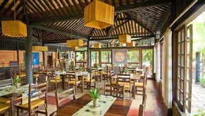 Un restaurante espacioso con mesas y sillas de madera, lámparas colgantes y amplias ventanas que dejan entrar la luz natural.