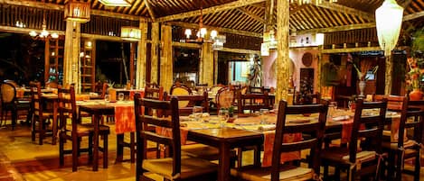Un restaurante con mesas y sillas de madera, faroles colgantes y suelo de baldosas.