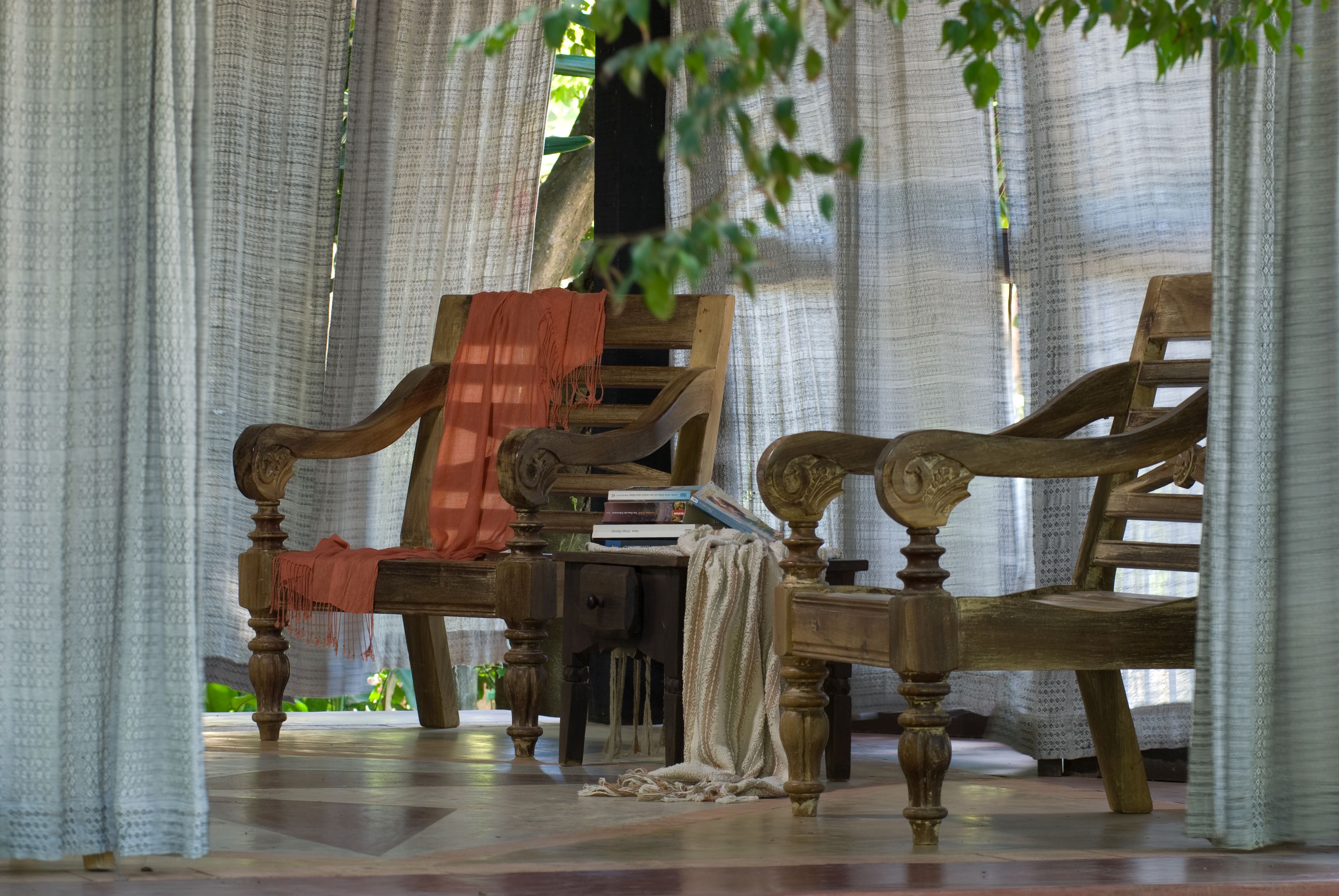 Une pièce avec une chaise en bois, une petite table et une fenêtre avec des rideaux.