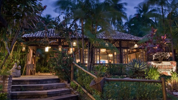 Un resort tropical con una estructura de madera tradicional, una escalera que lleva a la entrada y exuberante vegetación.