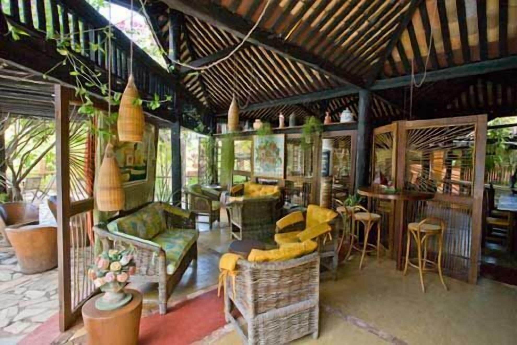 Un espacio interior con muebles de mimbre, plantas colgantes y un techo de paja.