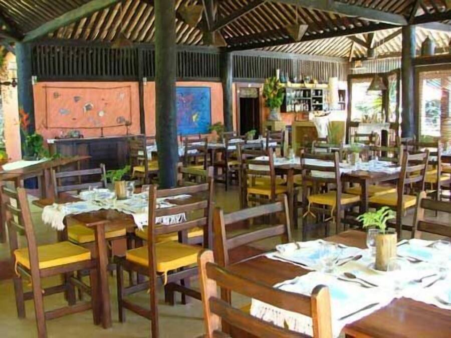 Ein Restaurant mit Holztischen und -stühlen, einige mit gelben Kissen.