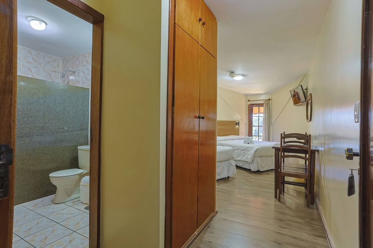 A hotel room with a wooden wardrobe, a bed, a chair, and a bathroom with a toilet and shower.