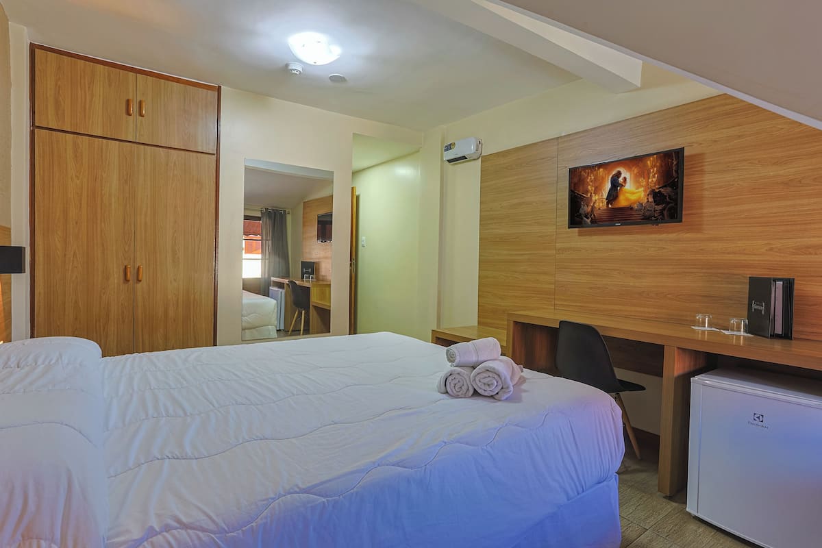 A hotel room with a large bed, a desk, a television, and a mini-fridge.
