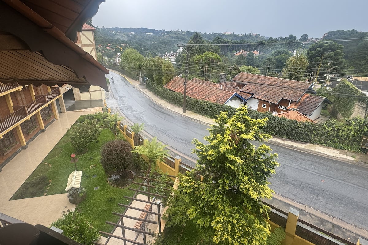 A view from a balcony overlooking a street with houses, a clear sky, and greenery.
