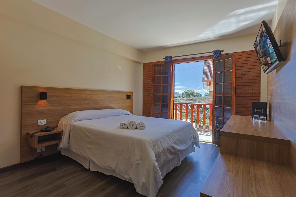 A bedroom with a bed, a nightstand, a desk, and a TV.