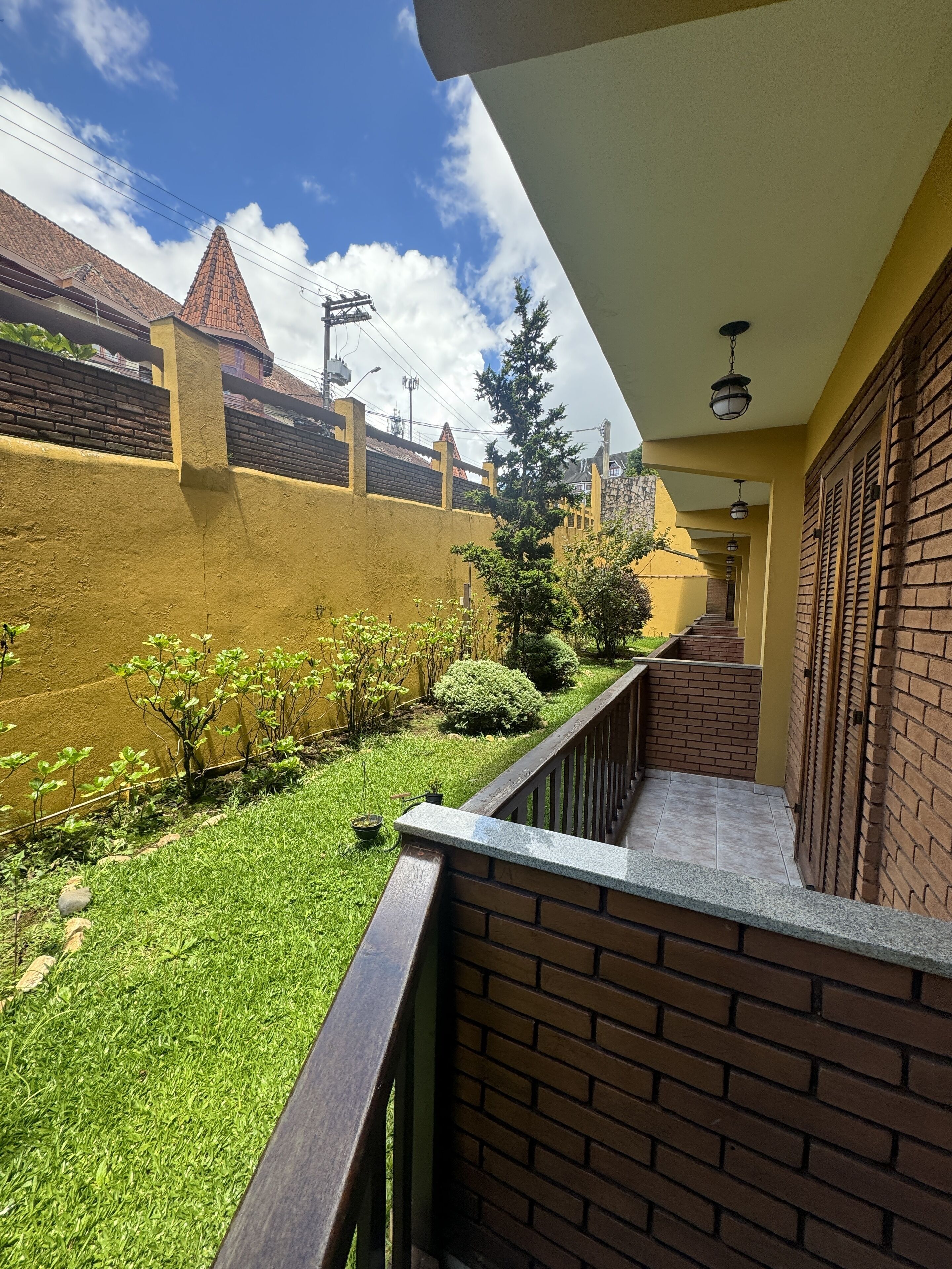 A balcony with a view of a brick wall, a small garden, and a staircase leading to a door.