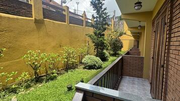 A balcony with a view of a brick wall, a small garden, and a staircase leading to a door.