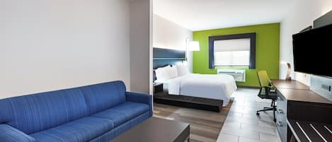 Ein Hotelzimmer mit blauem Sofa, einem Bett, einem Schreibtisch mit Stuhl und einem Fernseher.