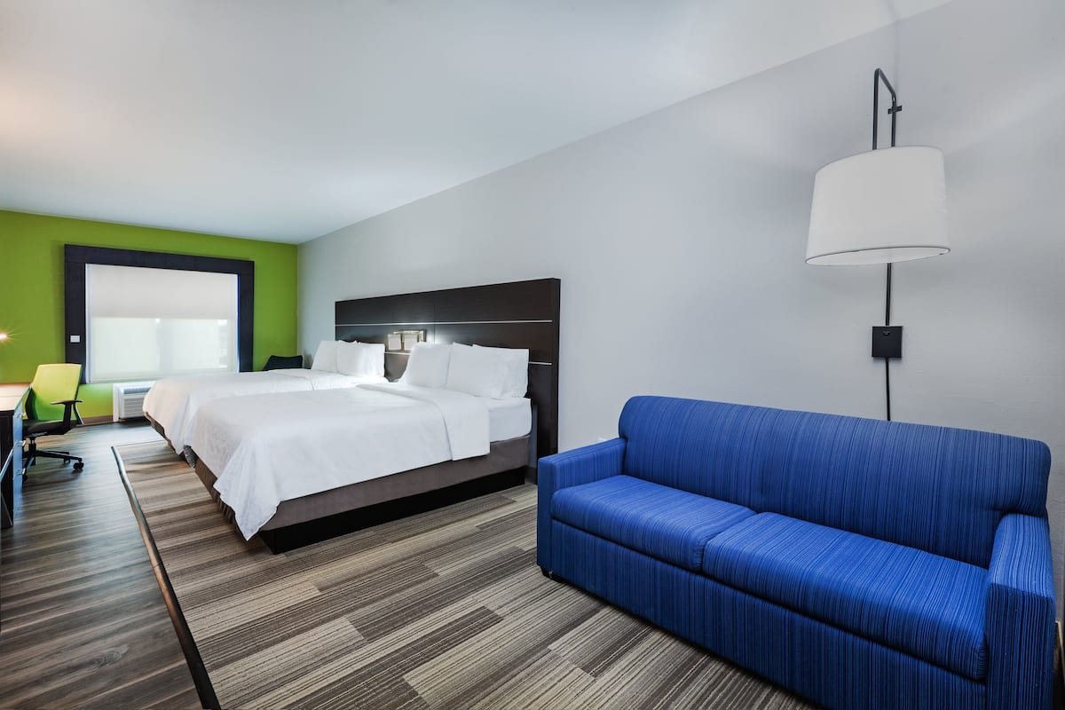 A hotel room with a bed, a blue sofa, a desk with a chair, and a lamp.