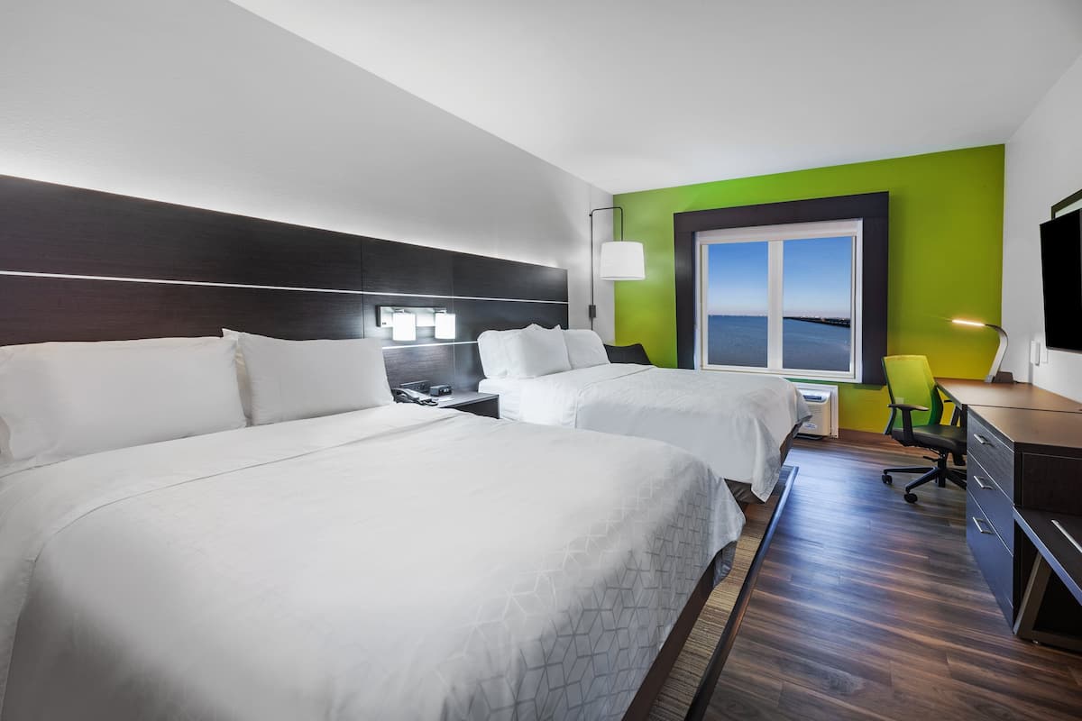 A hotel room with two beds, a desk, a chair, and a large window with a view.