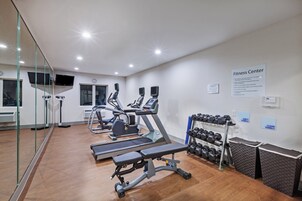 Un gimnasio con equipo de ejercicio, un televisor y un cartel que indica normas y responsabilidades.