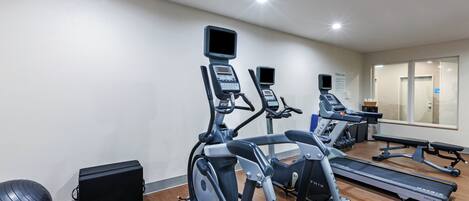Un gimnasio con cintas de correr, elípticas y una máquina de remo.