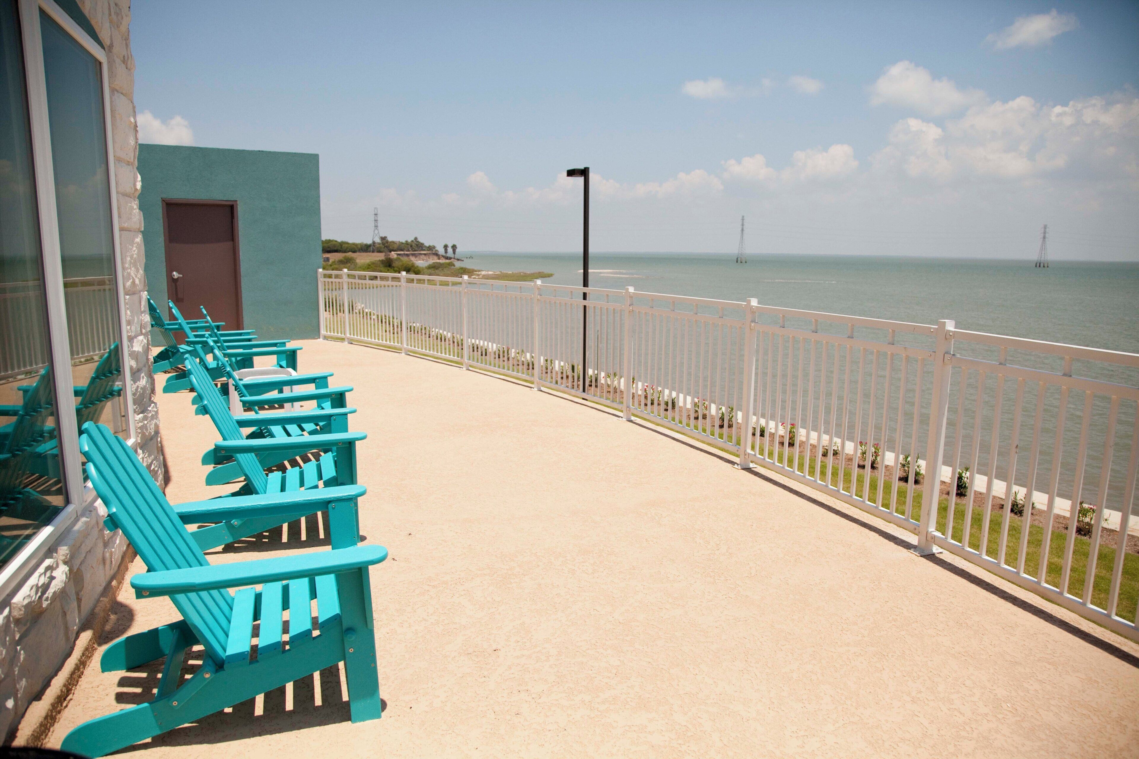 A balcony with turquoise chairs and a view of the sea.