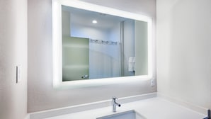 Une salle de bain moderne avec un grand miroir, un lavabo blanc et un espace douche.