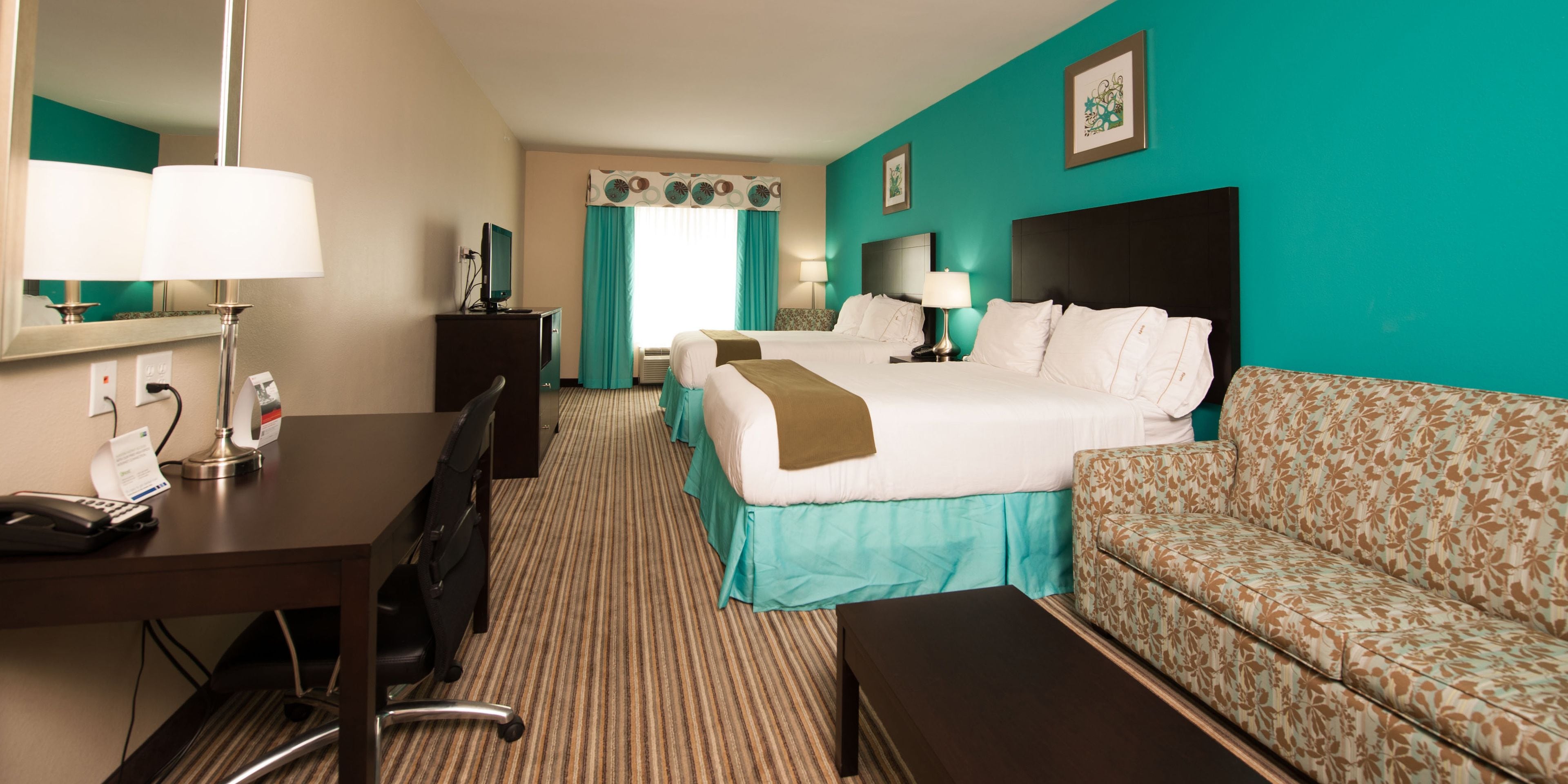 A hotel room with a bed, a desk with a telephone, a chair, a sofa, and a mirror.