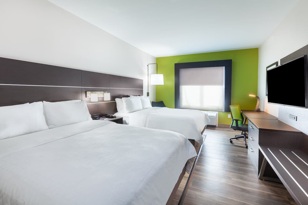 A hotel room with two beds, a desk, a chair, a TV, and a window with blinds.
