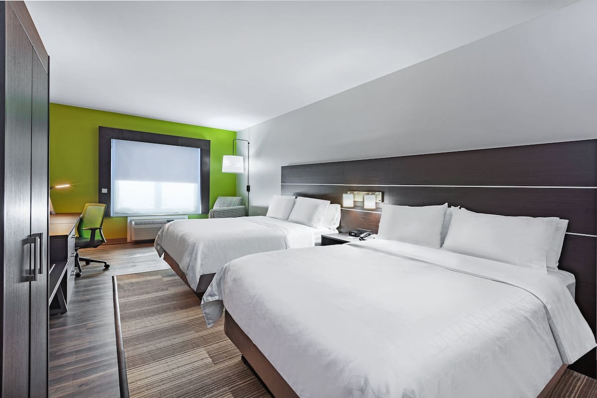 A hotel room with two beds, a desk, a chair, and a large window.
