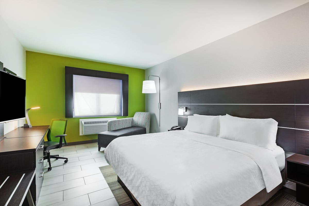 A modern hotel room with a large bed, a desk with a chair, a flat-screen TV, and a window with natural light.