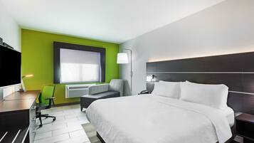 A modern hotel room with a large bed, a desk with a chair, a flat-screen TV, and a window with natural light.