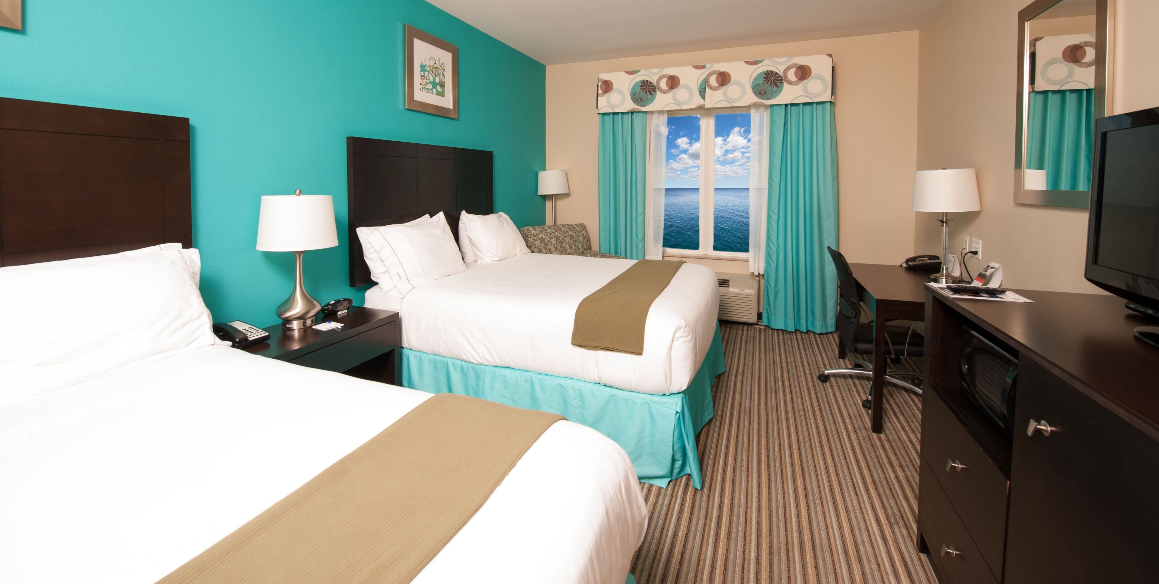 Une chambre d’hôtel avec deux lits, un bureau, une chaise, une télévision et une fenêtre donnant sur la mer.