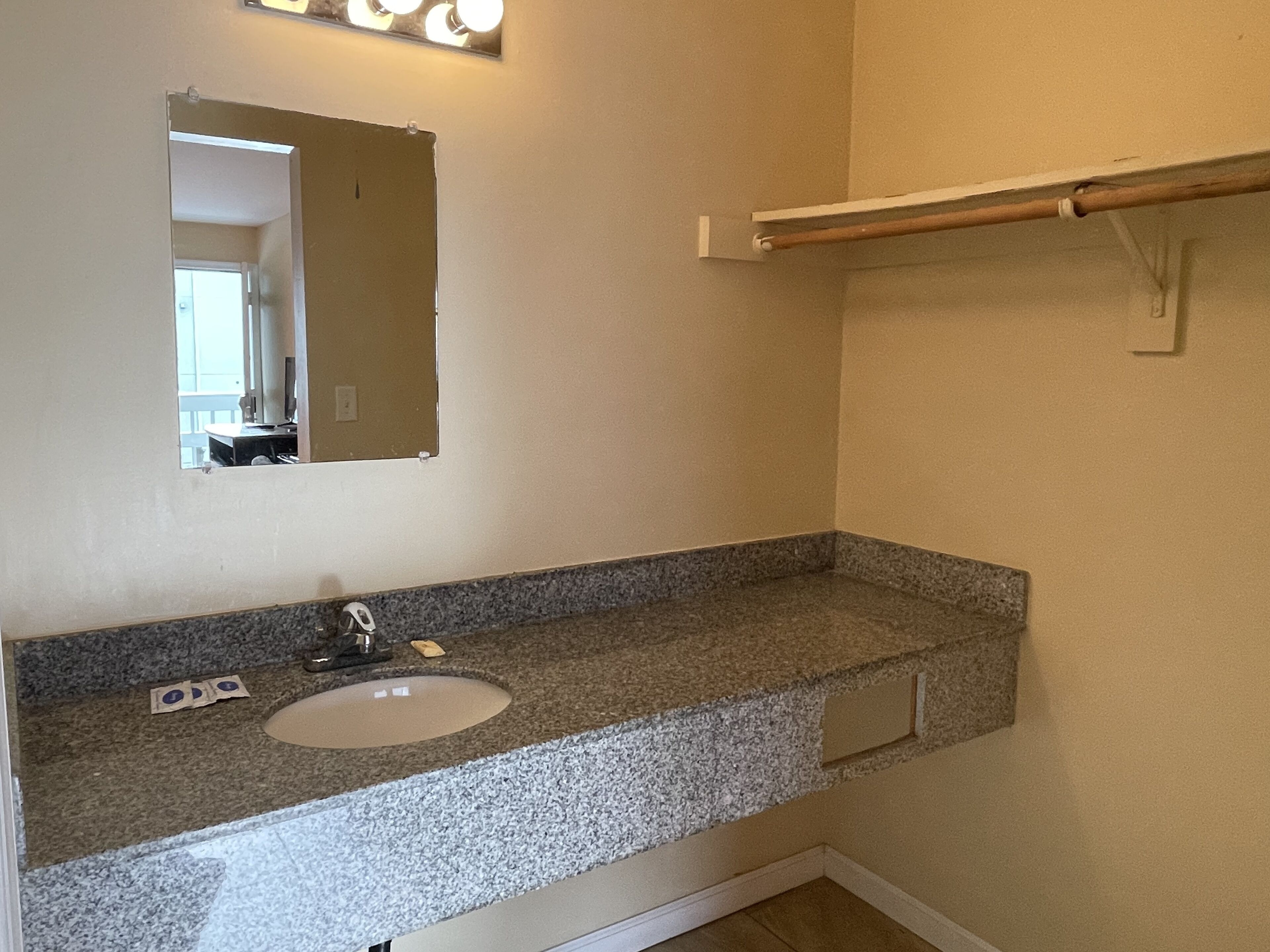 A bathroom with a granite countertop, a sink, a mirror, and a towel rack.