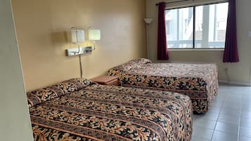 A hotel room with two beds, a nightstand, a lamp, and a window with curtains.