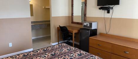 Una habitación de hotel con cama, escritorio, refrigerador, cómoda, televisor y espejo.