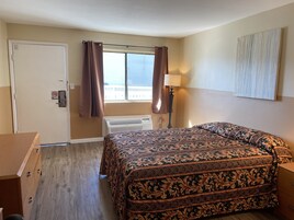 Habitación de hotel con cama, cómoda, lámpara y vistas a la ciudad desde la ventana.