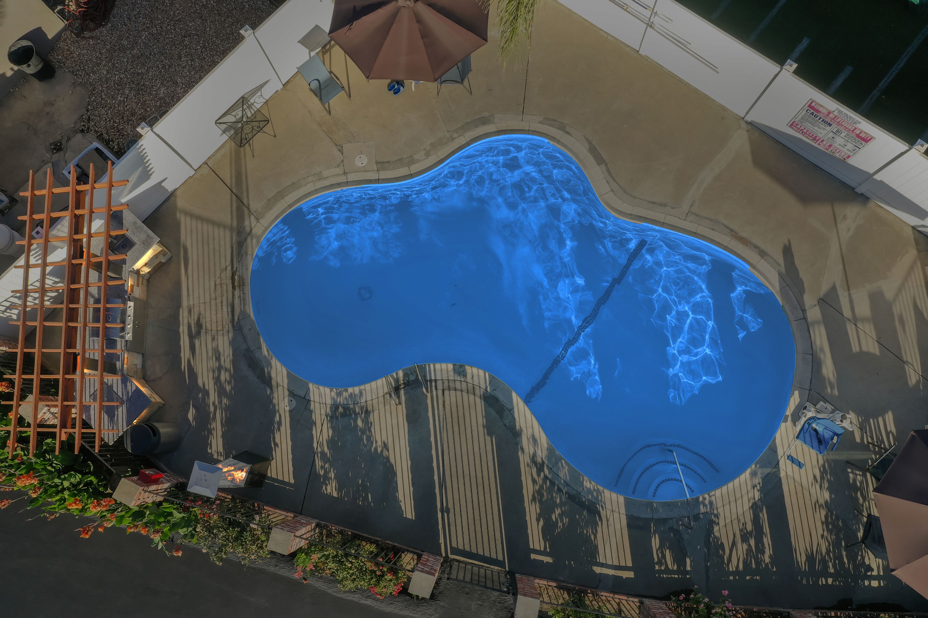 Luchtbeeld van een zwembad met een houten terras, een zwemtrap en een omheining.