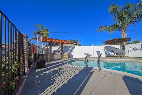 Une piscine avec une terrasse, une pergola et du mobilier d’extérieur.
