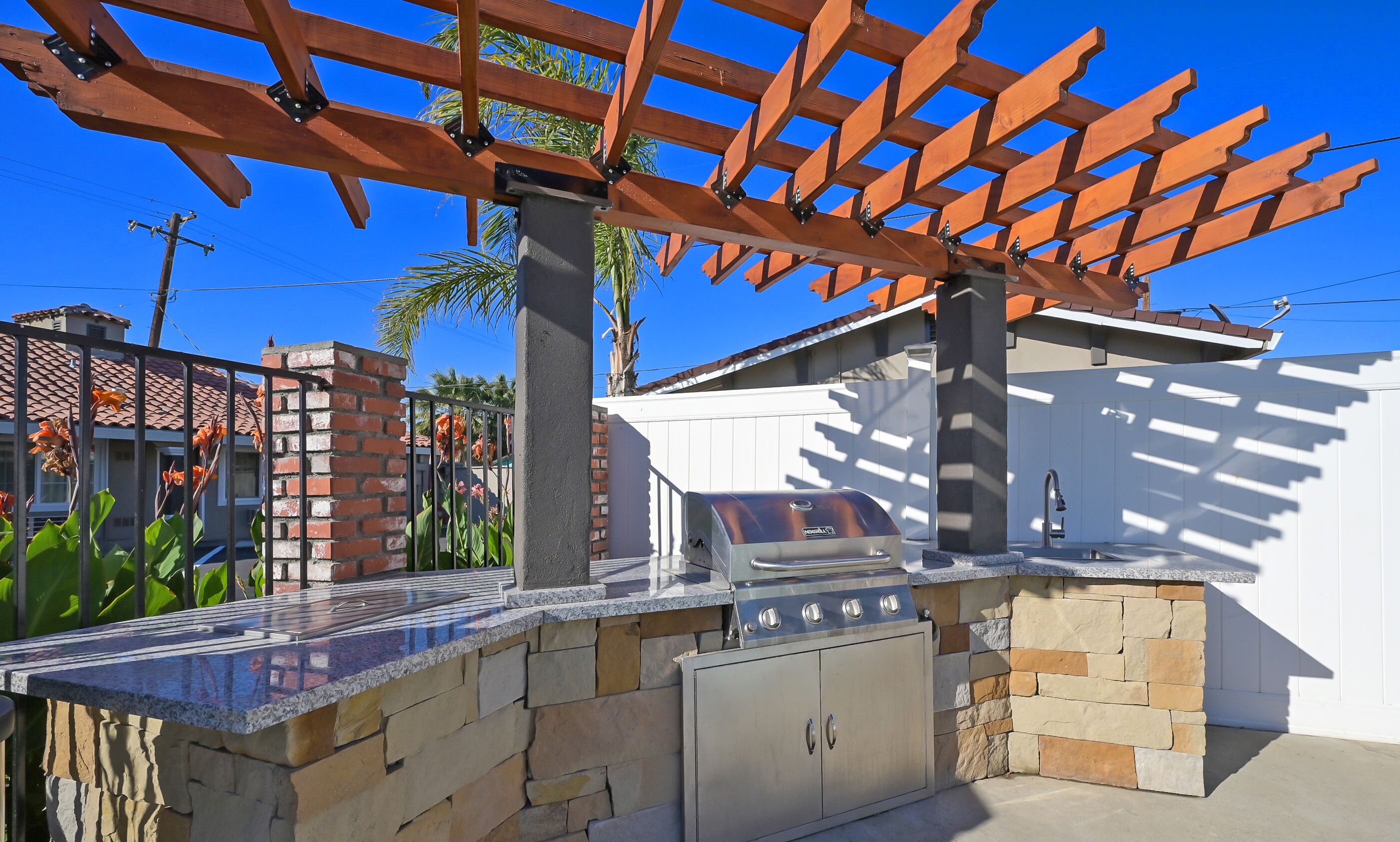 Cocina exterior con encimera de piedra, parrilla integrada y una pérgola.