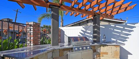 An outdoor kitchen with a stone countertop, a built-in grill, and a pergola overhead.